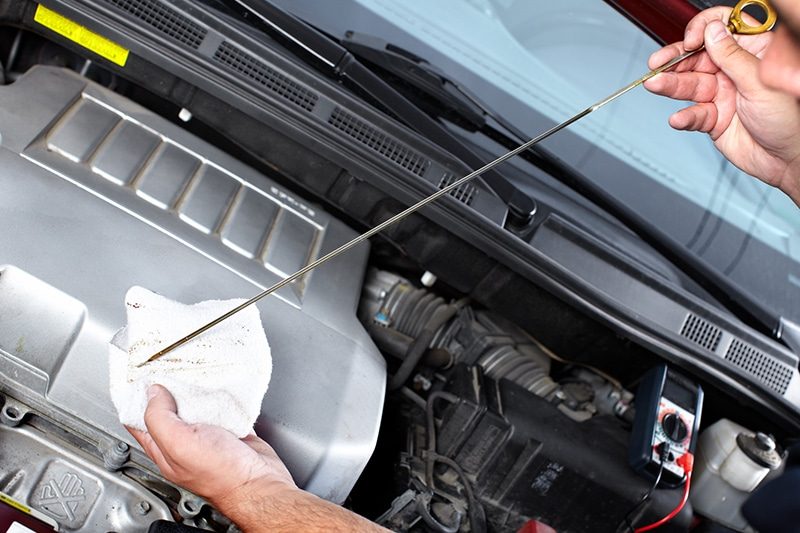 A technician checking engine fluid with a multimeter on the fender
