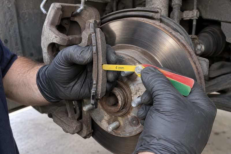 A technician measuring brake pad thickness at Dakota Ridge Auto